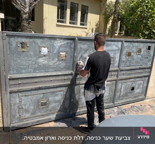 אדם צובע שער מתכת בצבע אפור עם רולר צבע